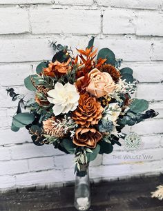 a vase filled with lots of flowers sitting on top of a wooden table next to a white brick wall