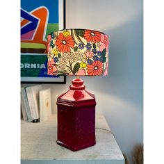 a red lamp sitting on top of a table next to a book shelf and painting