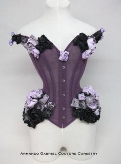 Twilight Rose is an enchanting, off the shoulder corset. Delicate, yet sturdy, it is supported by spiral and flat steel bones. The front has a steel busk, whilst the back laces permit size adjustments. The back has a modesty panel. The corset is made from strong mesh, covered by several layers of lilac and purple tulle.  Individually, hand folded and painted, cotton origami roses are applied on the hip, bust and shoulder areas.  This item is ideal for the following natural measurements: Waist: 6 Gothic Purple Corset With Corset Back, Fitted Gothic Purple Corset, Fitted Purple Corset With Boned Bodice, Purple Fitted Underbust Corset, Purple Underbust Corset Dress, Purple Corset Dress With Underbust Design, Purple Strapless Fitted Corset Dress, Purple Underbust Corset Dress With Corset Back, Gothic Fitted Corset For Dance