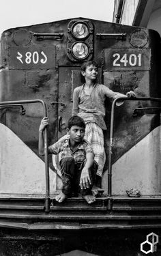 two young boys sitting on the front of a blue and yellow train with their arms around each other