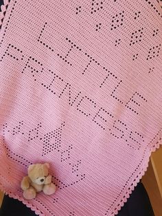 a teddy bear sitting on top of a pink crocheted blanket next to a black chair