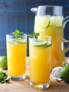 two glasses filled with lemonade and limes on top of a wooden cutting board