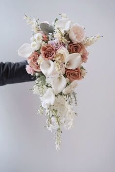 a person holding a bouquet of flowers with white and pink roses on it's side