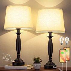 two lamps sitting on top of a wooden table next to a phone and remote control