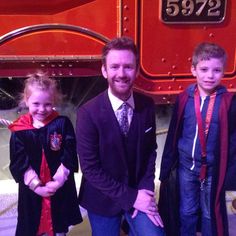 two boys and a girl are standing in front of a red train with harry potter on it