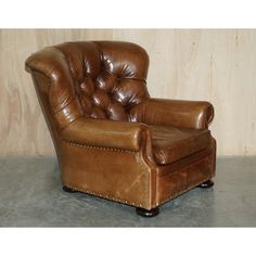 a brown leather chair sitting on top of a cement floor next to a wooden wall