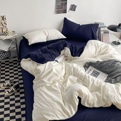 an unmade bed with blue sheets and white blankets on it, next to a black and white checkered floor