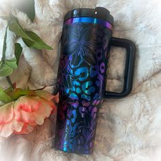 a purple and blue floral pattern on a black travel mug next to a pink flower