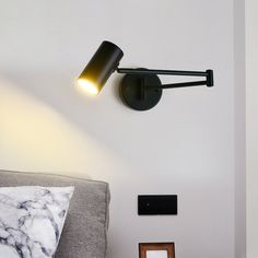 a black wall light mounted on the side of a white wall next to a bed