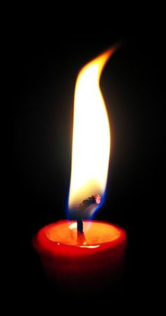 a red candle with a white flame is lit up in the dark, and it appears to be bright