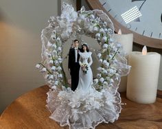 a bride and groom figurine sitting on top of a table next to a clock