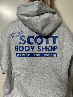 a person wearing a gray hoodie with the words scott body shop on it's back