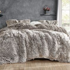 a bed with grey fur on it in a room next to a window and wooden floor