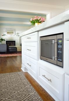 a kitchen with white cabinets and stainless steel microwave on the wall, along with a floral centerpiece