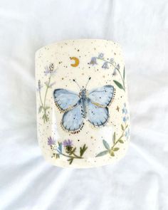 a blue butterfly is sitting on top of a white cup with flowers and stars around it