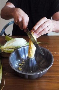 a man is cutting corn on the cob with a large metal bowl and knife