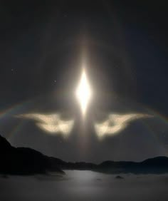 two angel wings in the sky with a bright halo above them and mountains behind it