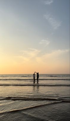 two people standing in the ocean at sunset