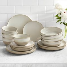 a table topped with lots of white plates and bowls next to a vase filled with flowers