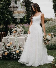 a woman in a wedding dress standing next to a table with flowers and chandeliers