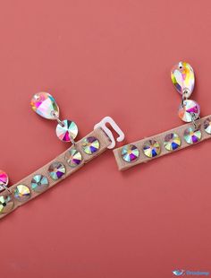 a pair of bracelets with colorful stones on them sitting on a pink surface next to an earring