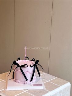 a pink and black birthday cake on top of a white table with a lit candle