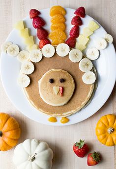 a plate with pancakes and fruit on it that has a turkey face made out of bananas