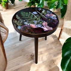 a table with flowers painted on it in front of some potted plants and wicker chairs