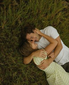 a man and woman laying in the grass with their arms around each other as they cuddle