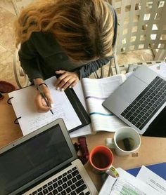 a woman sitting at a table with two laptops and papers