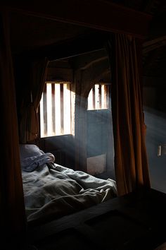 the sun shines through two windows onto a bed in a dark room with drapes