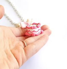 a hand holding a tiny pink and white cake necklace