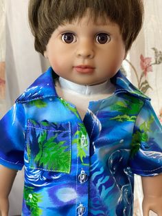 a close up of a doll wearing a blue shirt with green leaves on it's chest