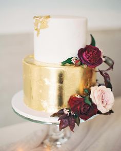 a white and gold wedding cake with red flowers on the top tier, sitting on a table