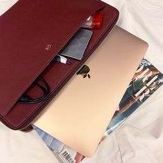 an open laptop computer sitting on top of a white bed next to a magazine and other items