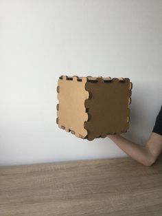 a person holding up a piece of cardboard that is shaped like a puzzle box on the wall