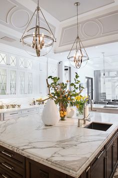 a kitchen with marble counter tops and an island in front of the sink, lights hanging from the ceiling