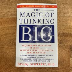 the book is sitting on top of a wooden table and it says, the magic of thinking big