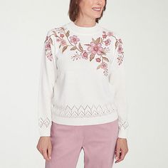 a woman wearing pink pants and a white sweater with flowers on the sleeves is standing in front of a white background