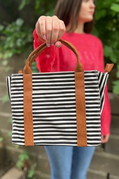 The cutest little midsize tote, this black and white striped canvas bag is accented with faux brown leather for a touch of sophistication. The roomy interior features a removable compartment organizer as well as a zippered pouch. Removable cross strap, single front slip pocket. Dimensions: 10" x 4.5" x 8.25" Black Rectangular Satchel With Canvas Lining, Everyday Striped Bags With Leather Handles, Black Satchel With Canvas Lining For Daily Use, Chic Black Canvas Bag For On-the-go, Brown Travel Bag With Striped Lining, Everyday Striped Canvas Bag, Chic Black Canvas Satchel, Everyday Tote Canvas Bag With Striped Lining, Black Travel Bag With Striped Lining