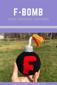 a hand holding up a crocheted ball with the letter f on it, in front of a grassy field