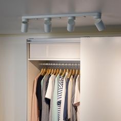 an open closet with clothes hanging on rails and two lights above the closet door,