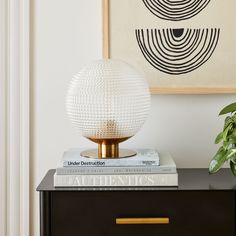 a black and gold side table with two books on it next to a white plant