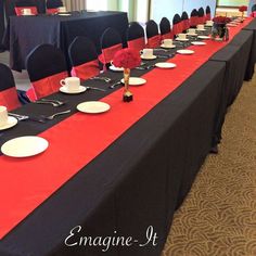 a long table is set up with black and red linens, white plates and silverware