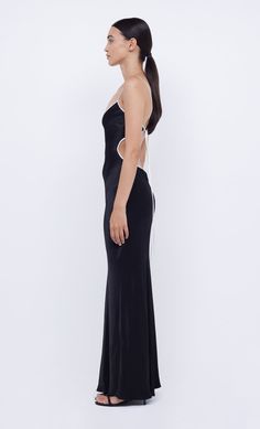 a woman in a long black dress with one shoulder cut out, looking off to the side