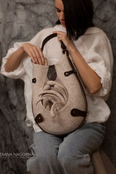 a woman sitting on a chair holding a handbag in front of her face and looking at the camera