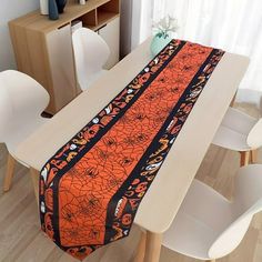 an orange and black table runner sitting on top of a wooden table next to white chairs