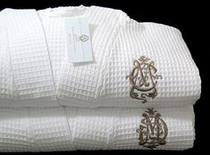 two white towels with gold embroidered monogrammed letters on them, one folded and the other rolled up