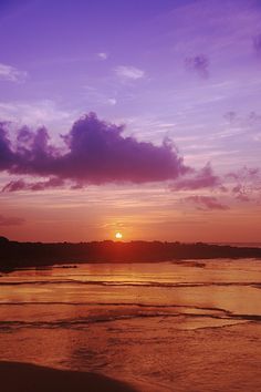 the sun is setting over the ocean with clouds in the sky and water on the beach