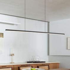 a dining room table and chairs in front of a white wall with hanging lights above it